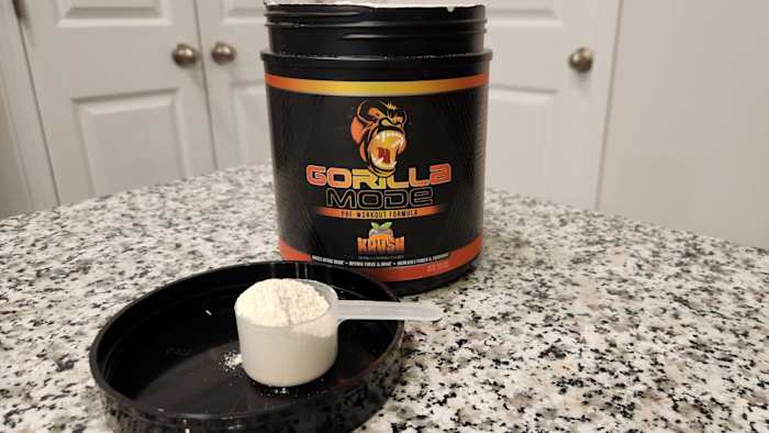 A black container of Gorilla Mode pre-workout powder in Orange Krush flavor on a kitchen counter